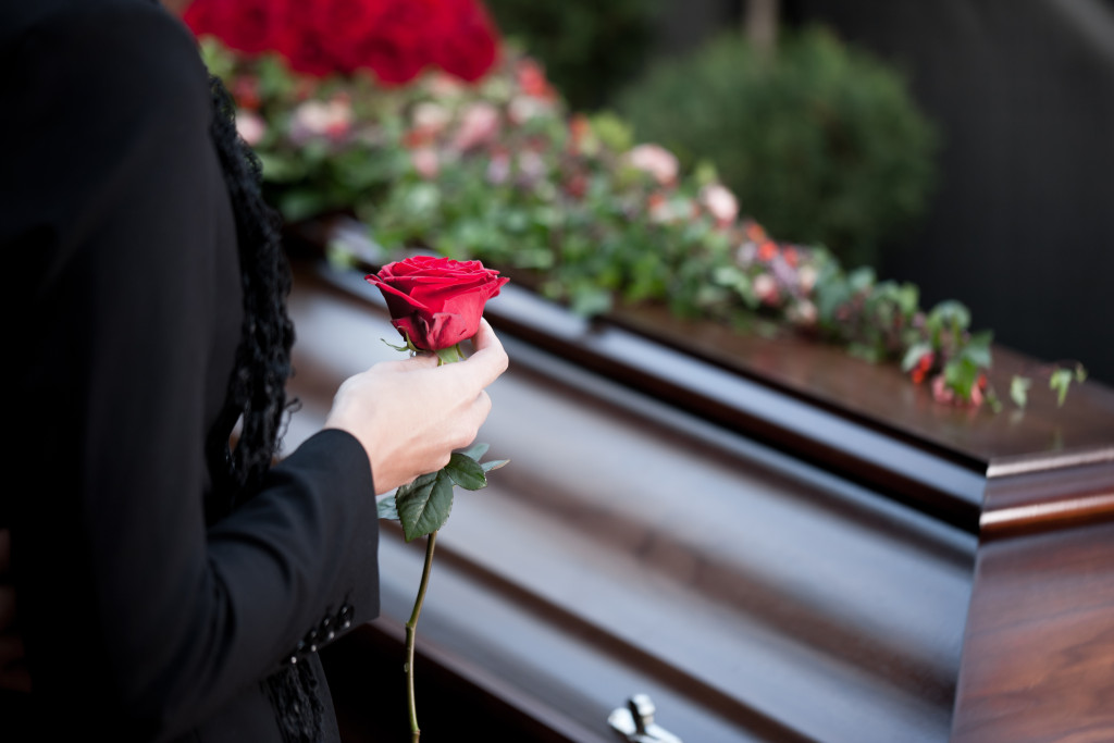 woman laying rose on coffin