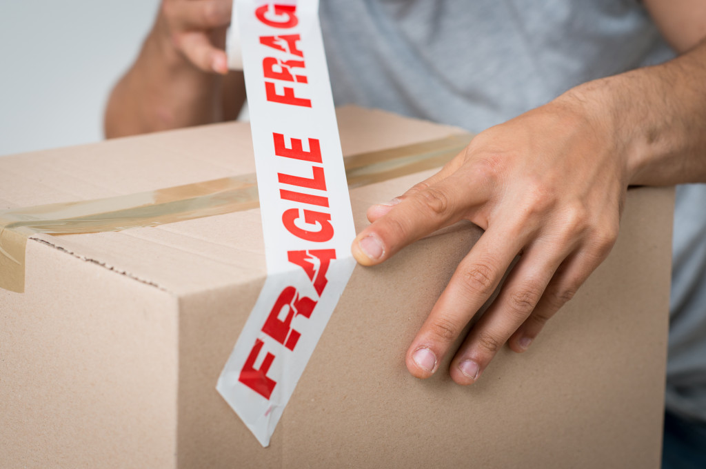 A person putting applying a tape saying fragile on a cardboard box