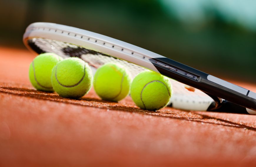 Tennis racket and tennis balls on the ground of a clay tennis court.