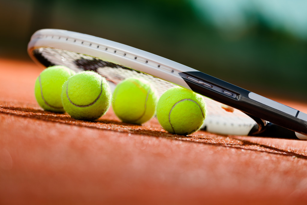 Tennis racket and tennis balls on the ground of a clay tennis court.