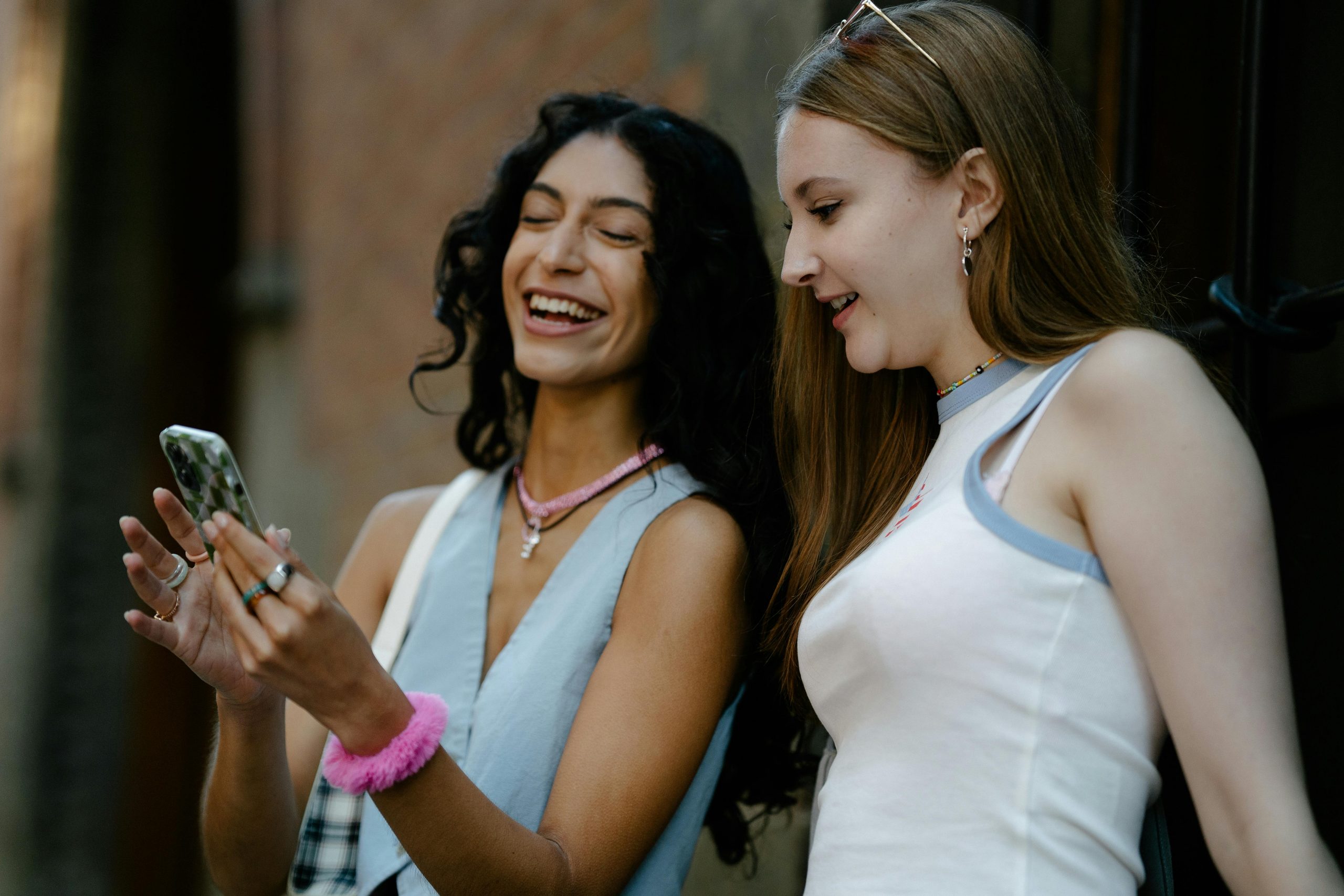 two women smiling as they look at a phone screen